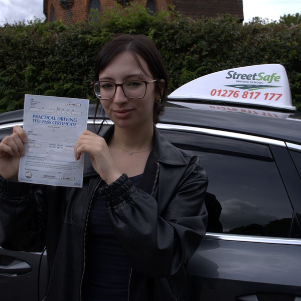 student holding practical driving test pass certificate and standing by StreetSafe Driving School car